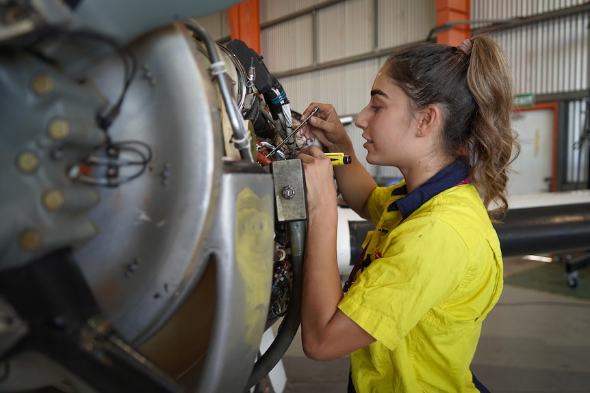 A woman shines a torch light into the wiring of an aircraft as she examines the plane for maintenance