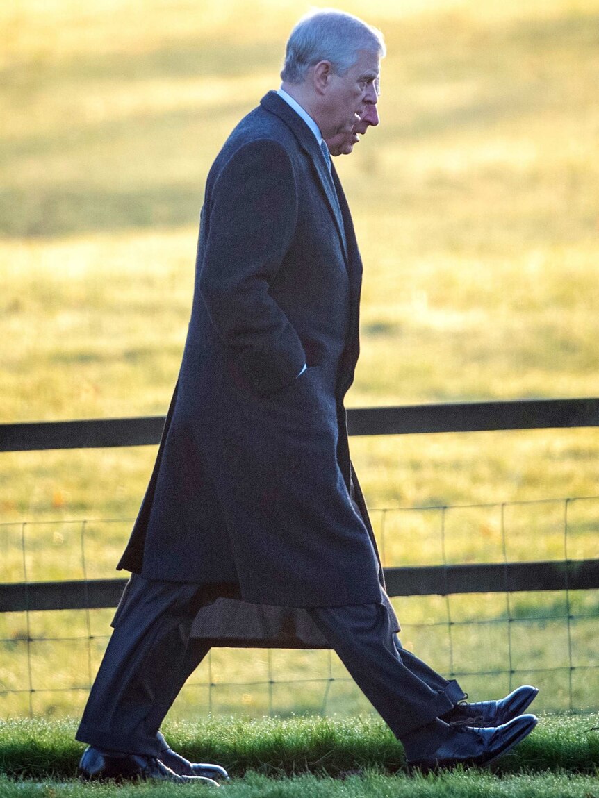 Prince Andrew walks along a path in front of a green paddock with Prince Charles beside him.