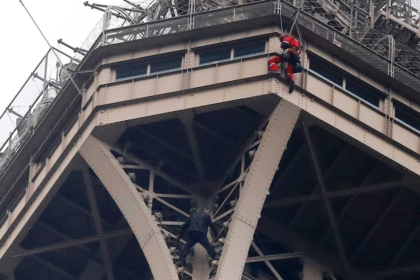 A rescue worker hangs from the Eiffel Tower while a climber is seen below him.