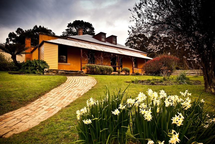 picture of an old cottage with green grass and daffodils out the front