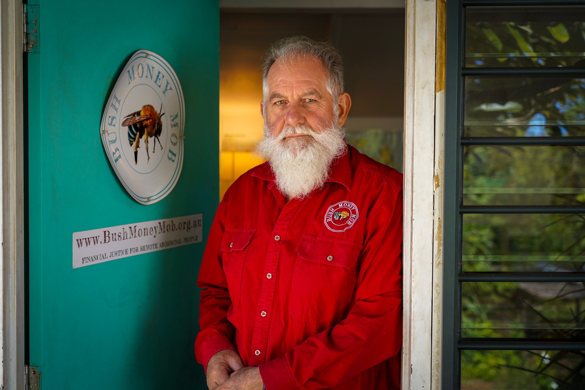 A bearded man in a red shirt standing in a doorway