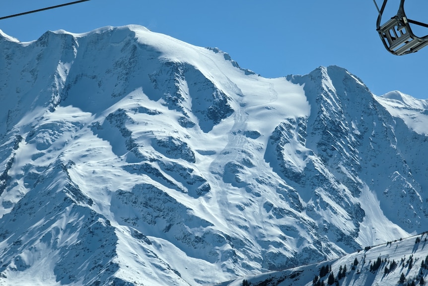 A large alp is covered in snow with a thin trail of disturbed snow showing the path of an avalanche that ran between ridges.