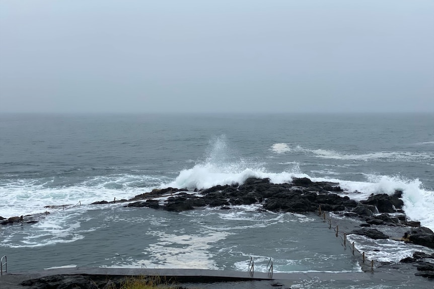 Irregular-shaped pool cut into natural rock surrounding by breaking waves and ocean foam