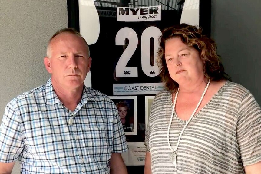 A man and a woman in front of a framed football guernsey.