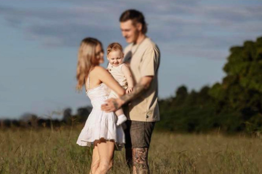 Baby Jarrod with parents Felicity and Josh in a field. The parents' faces are blurred for privacy