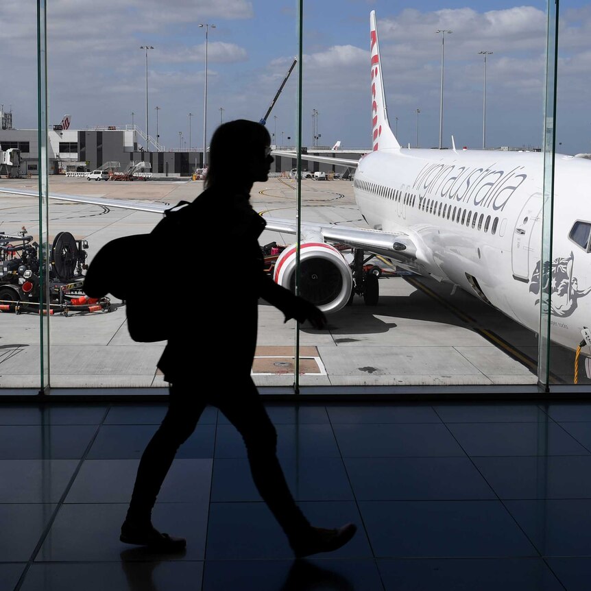 The photo shows the silhouette of a woman walking inside Melbourne Airport as a plane prepares for boarding.