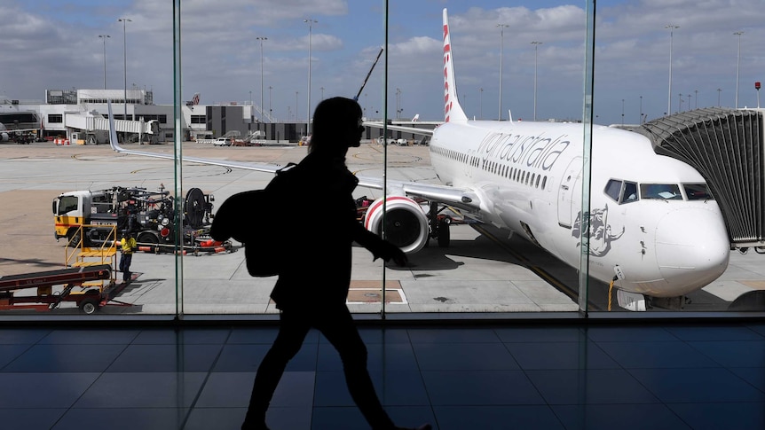 The photo shows the silhouette of a woman walking inside Melbourne Airport as a plane prepares for boarding.