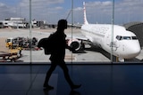 The photo shows the silhouette of a woman walking inside an Airport as a plane prepares for boarding.