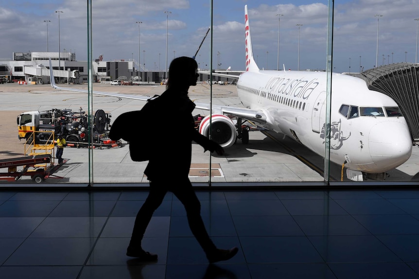 The photo shows the silhouette of a woman walking inside Melbourne Airport as a plane prepares for boarding.