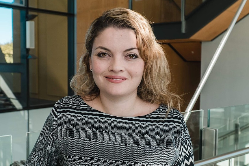 A close-up photograph of Dr Justine Gatt posing in front of a glass stairway