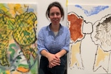 Artist Kate Smith sits in front of two painted canvases in an art space