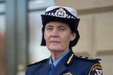 A woman wearing a blue police commissioner's uniform looks seriously at the camera. 