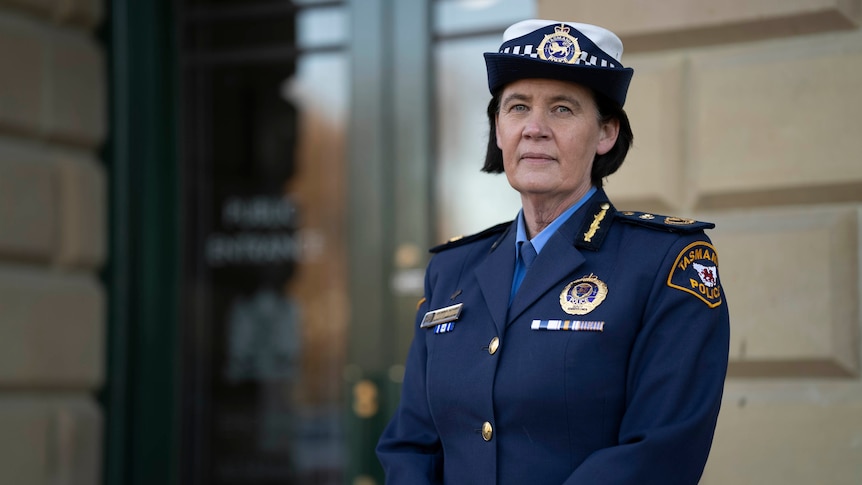 A woman wearing a blue police commissioner's uniform looks seriously at the camera. 