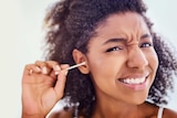 A woman winces as she cleans her ear with a cotton bud.