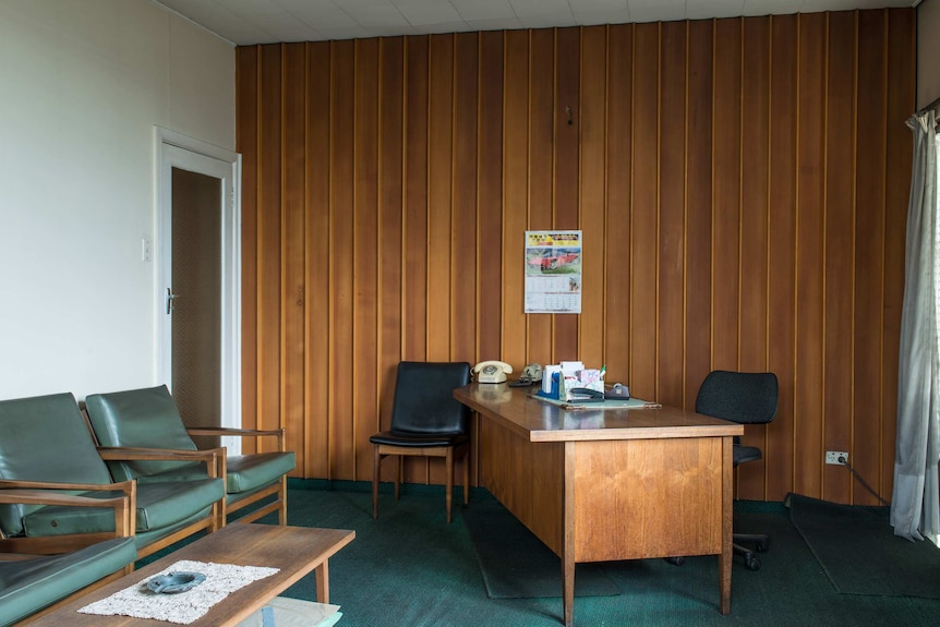 An empty office foyer and waiting room with green armchairs and an ashtray on the coffee table.