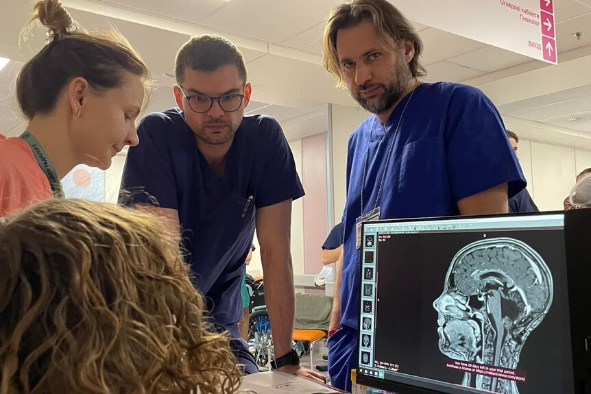 Four medical staff gather around a brain scan, Dr Dmytro Ishchenko in navy scrubs and glasses.