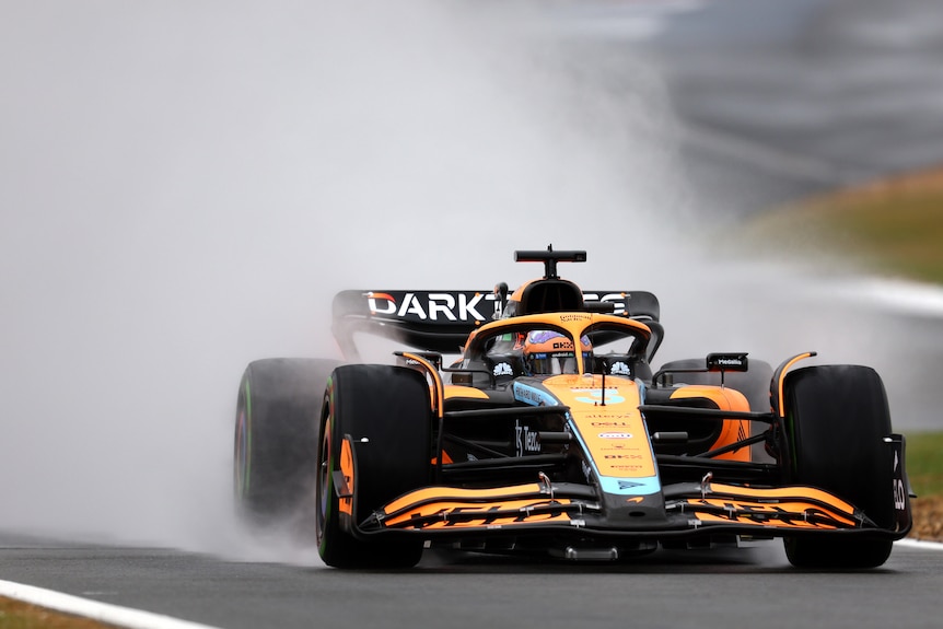 Water sprays from behind the tires of Daniel Ricciardo's McLaren car on track