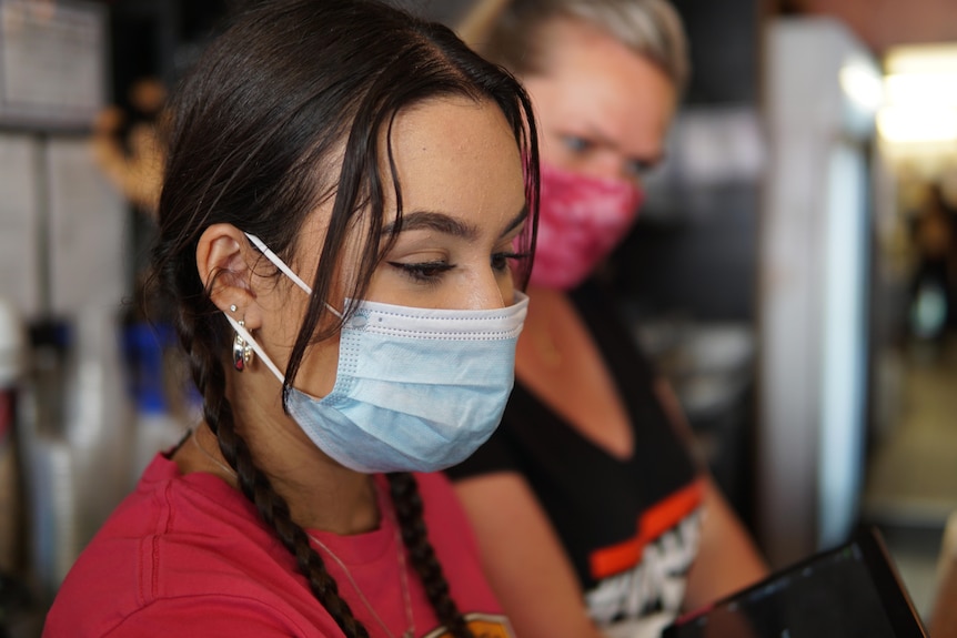 A young woman works the till as Siri looks on.