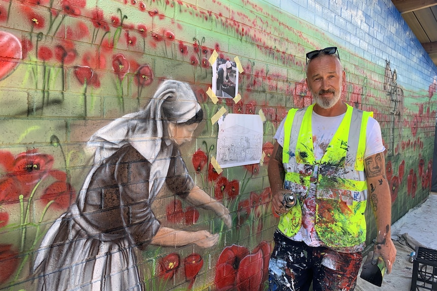 a muralist stands with spray paint in front of a mural of poppies.