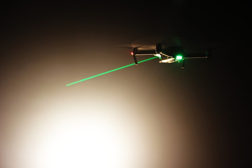 A drone hovers while a green laser appears pointed at it.