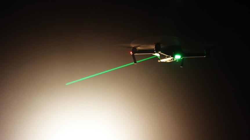 A drone hovers while a green laser appears pointed at it.