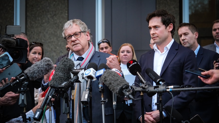 two men stand in front of microphones