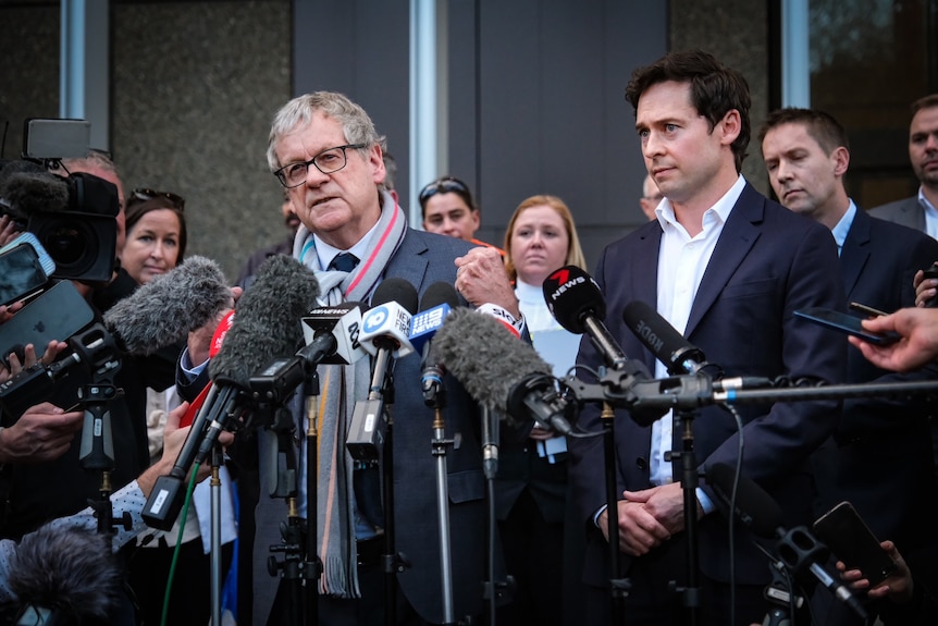 two men stand in front of microphones