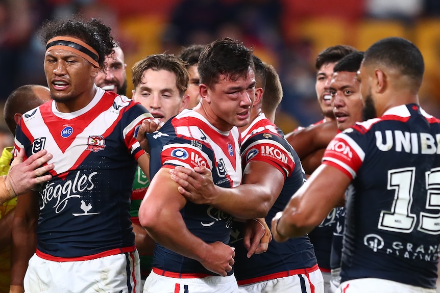 A Roosters NRL player stands near teammates with bad swelling on his cheek and below his eye.
