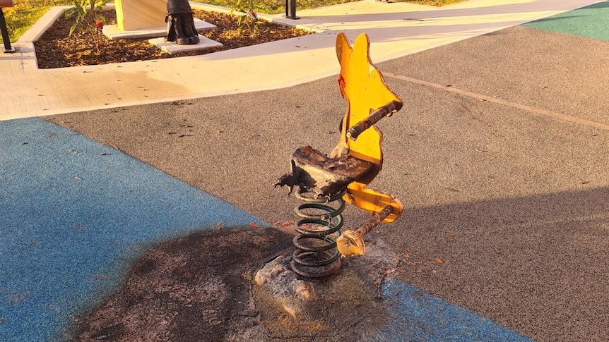 A burnt piece of play equipment stands on scorched soft flooring at the memorial playground