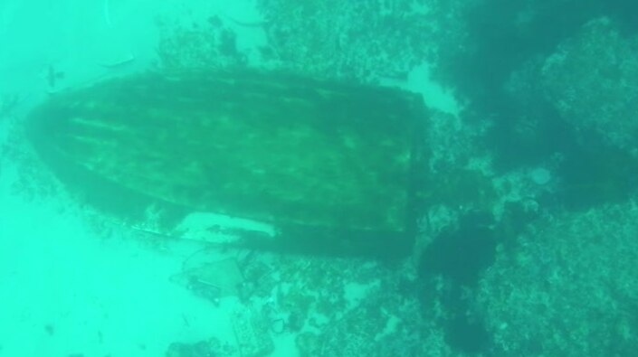 An underwater photo of the hull of a boat sitting upturned on the sea floor.
