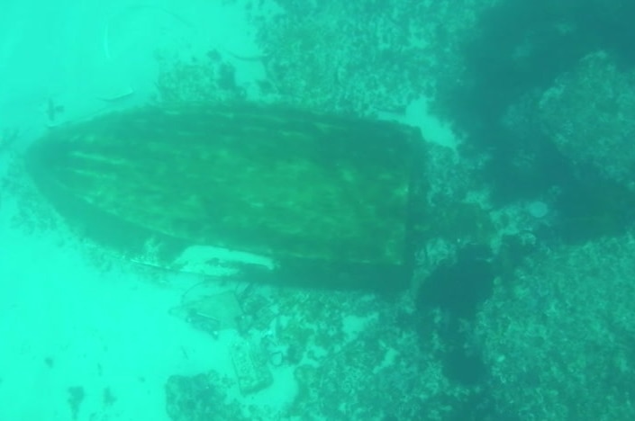 An underwater photo of the hull of a boat sitting upturned on the sea floor.