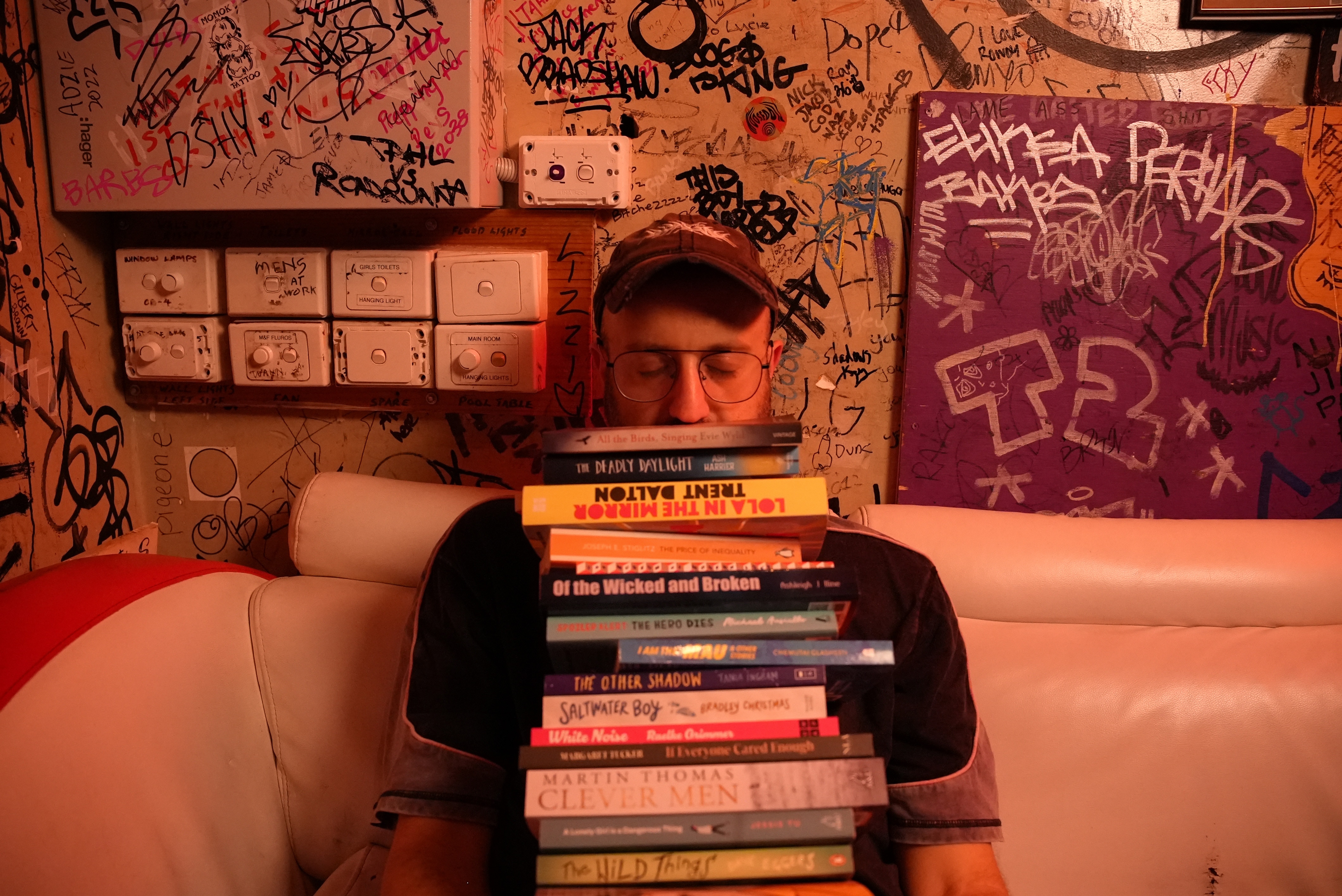 A man sitting down leaning his head on a pile of books, eyes closed, reading glasses