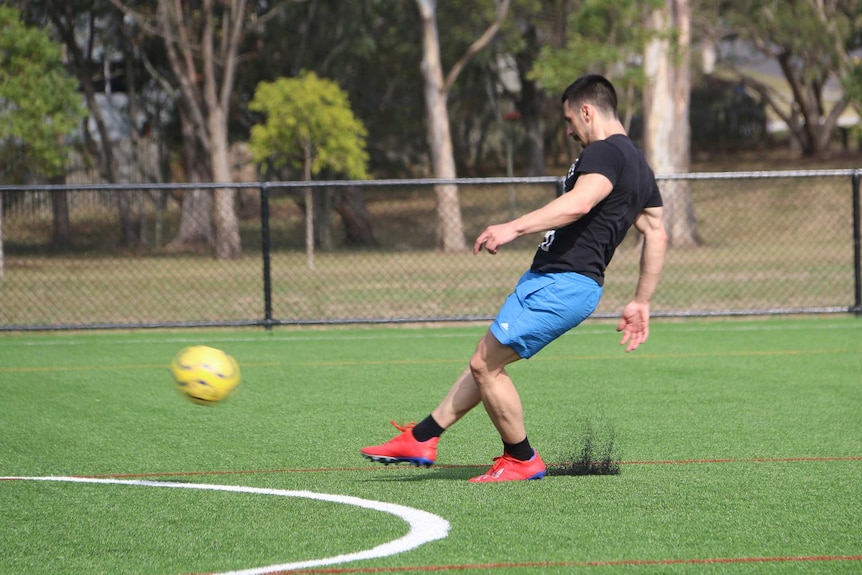 Dirt flies up from under the shoe of a soccer player as he kicks a ball on a synthetic pitch.