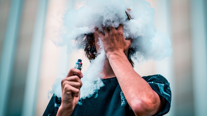 The face of a young man, who is holding a vape, is covered in vape smoke