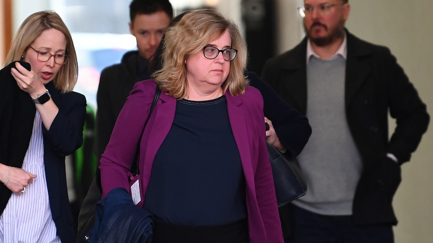 a woman in a purple jacket leaving court