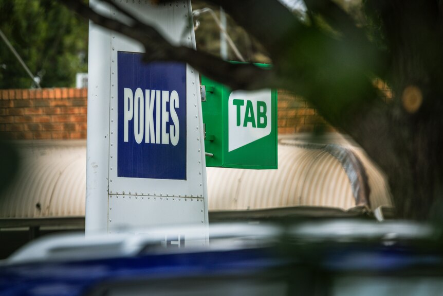 Signs above a building read 'pokies' and 'TAB'.