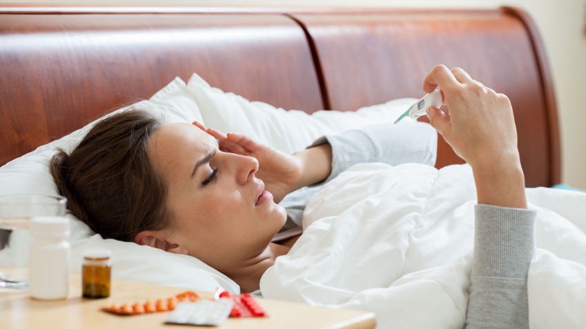 A woman lying in bed checking her temperature