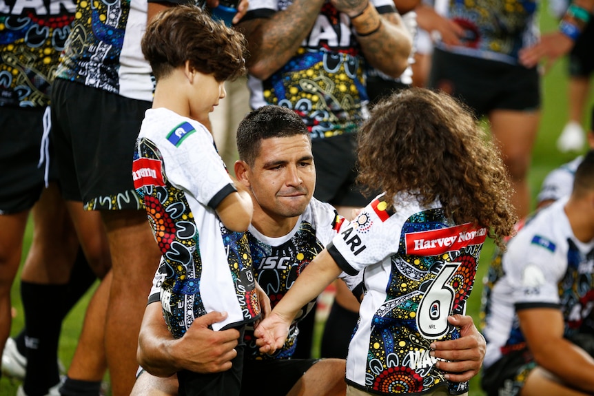 Cody Walker crouches down hugging his two children, standing up, with one in each arm