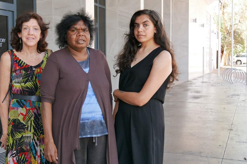 Three women stand outside a building and stare at the camera.