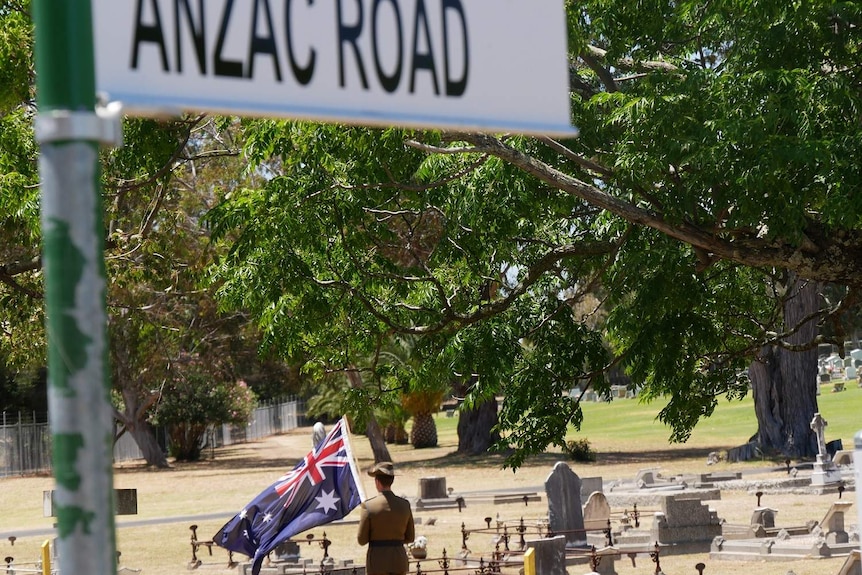 Soldier holds Australian flag behind street sign in cemetery
