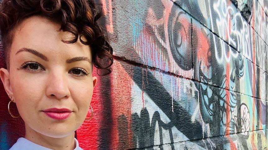 Sarah McCarthy smiles while standing in front of wall, for a story about telling workplaces about chronic health conditions.