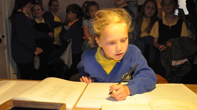 young girl in school uniform writing at a desk