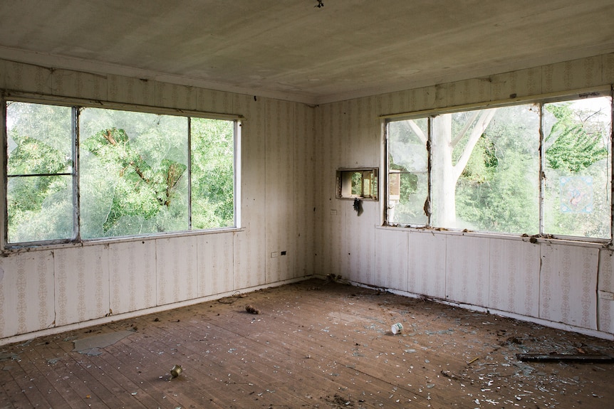 An empty room with retro wallpaper empty with windows missing and cobwebs. 