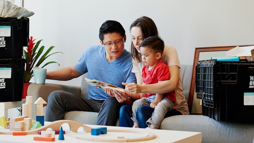 Family of three sitting on the couch in new rental home, in a story about how to find long-term rentals.