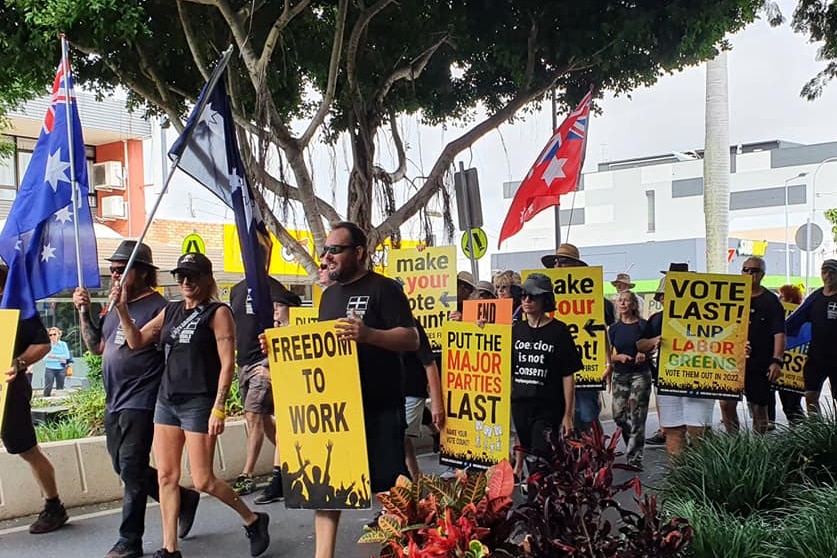 A group of people walking down a city street holding freedom signs and Australian flags.