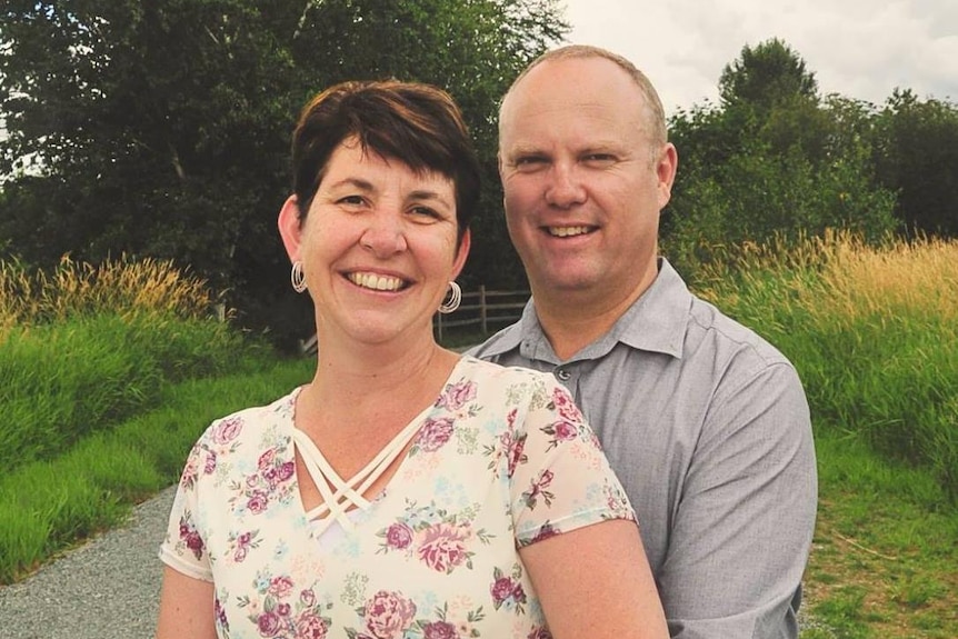 A woman in a floral dress poses for a photo with a man in a grey shirt