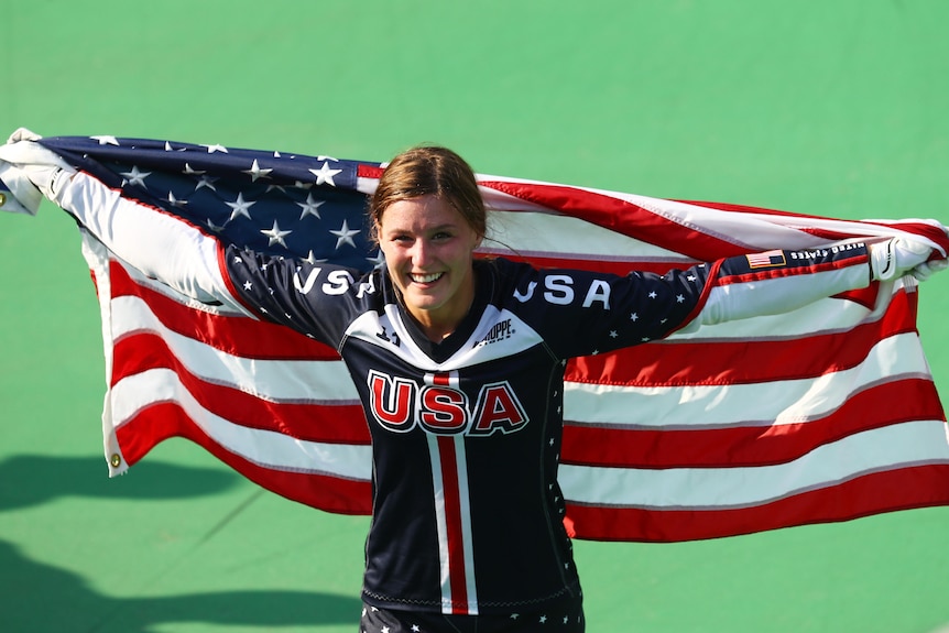 Alise Post holds up a USA flag behind her and smiles