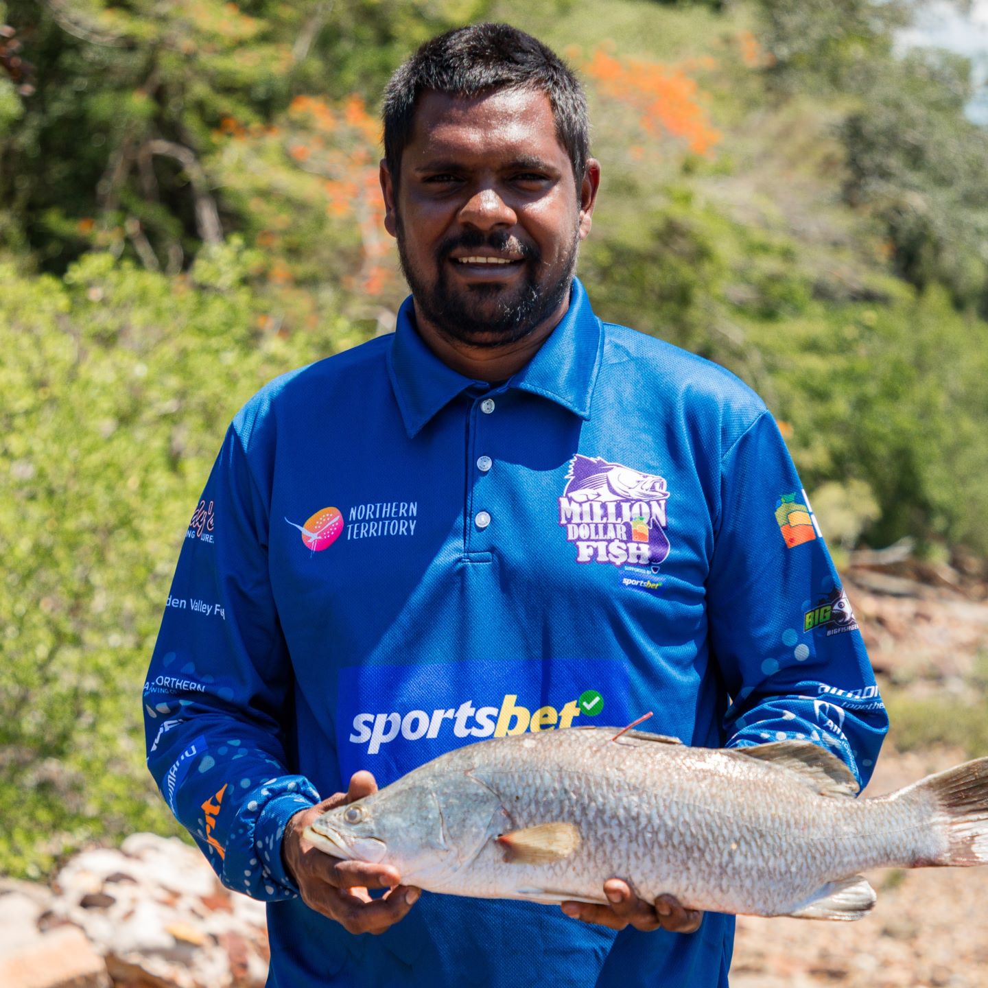 A man, Jack Daly, holding a tagged barramundi fish in a blue shirt