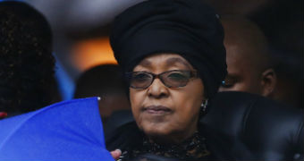 Winnie Madikizela-Mandela in a black headdress with a somber expression looks into the distance.