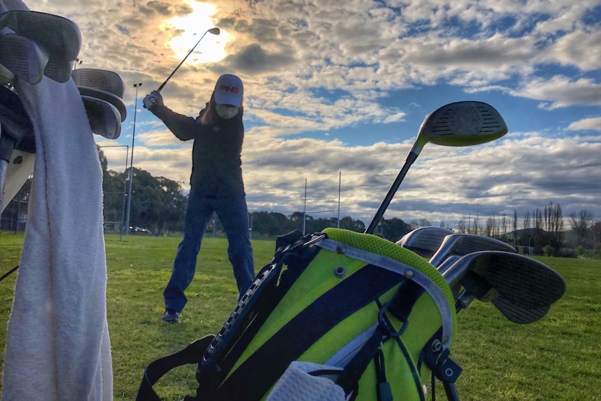 A person in a face mask swings a golf club.